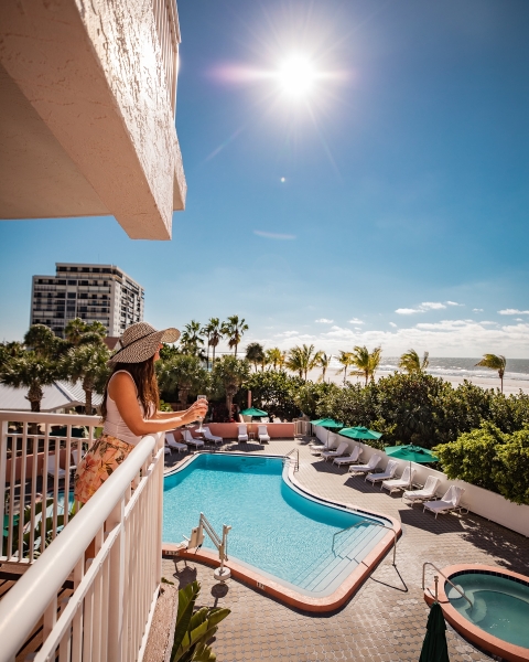 A woman on a balcony drinking champagne looking out over the pool