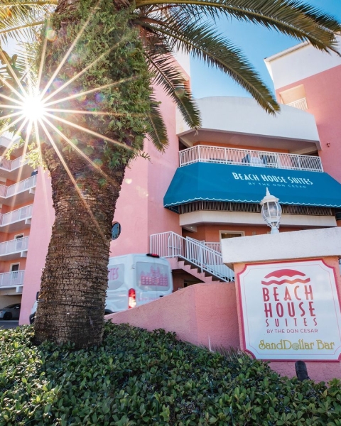 Entrance of the Beach House Suites with a palm tree in front and the sun shining bright